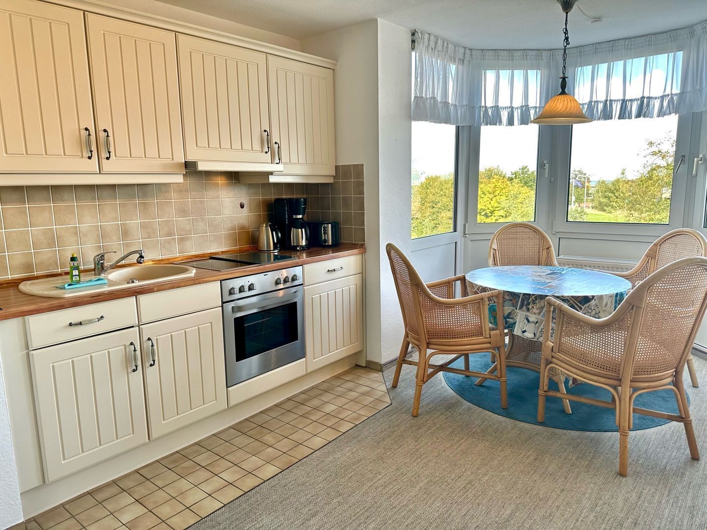 A kitchen with white cabinets, a stove, and a dining area with wicker chairs and a table.