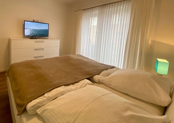 A bedroom with a bed, a TV on a dresser, and a window with curtains.