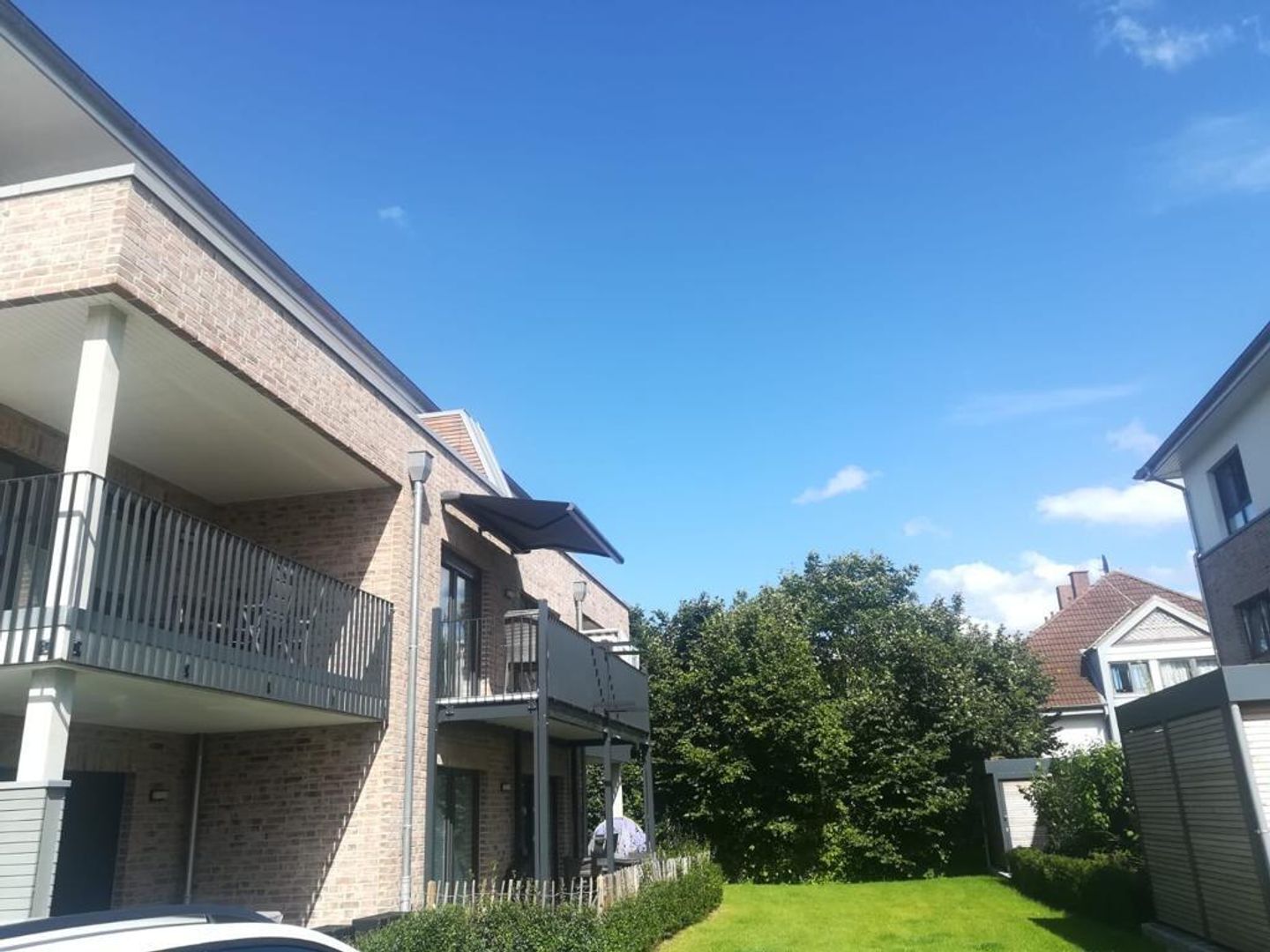 Un quartier résidentiel avec des maisons en briques, une pelouse verdoyante et un ciel bleu dégagé.