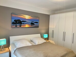 A bedroom with a bed, a nightstand, a wardrobe, and a sunset painting on the wall.