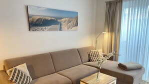 A modern living room with a beige sofa, a small wooden side table, and a painting of a beach scene.