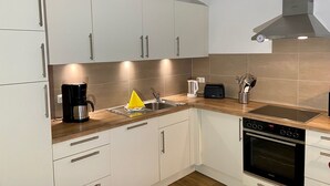 A modern kitchen with white cabinets, a stainless steel range hood, a built-in oven, and a coffee maker.