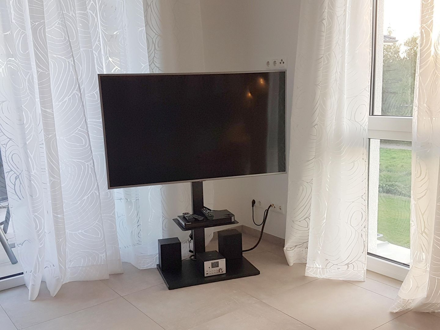 Un téléviseur à écran plat fixé sur un support, avec une télécommande et un câble d’alimentation.