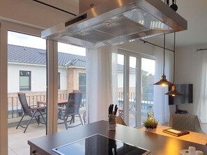 A modern kitchen with a large window, a built-in stove, and a dining area with chairs and a table. - 2405 - Sonnenbrook - Sonnenbrook in Dahme (Dahme)