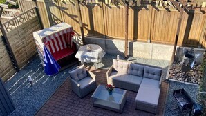 Un patio con mobiliario de mimbre, una mesita y una parrilla.