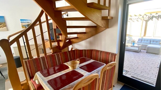 Un comedor con una escalera de madera, un banco acolchado a rayas y una mesa con manteles individuales.