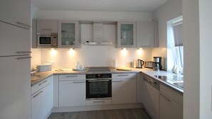 Cozinha compacta com armários brancos, forno embutido, micro-ondas e cafeteira.