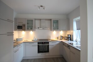 A compact kitchen with white cabinets, a built-in oven, a microwave, and a coffee maker.