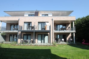 En moderne boligbygning i to etager med fladt tag, store vinduer og altaner.