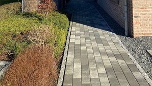 Um edifício moderno com fachada de tijolos, um caminho pavimentado e uma pequena área ajardinada.