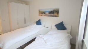 Quarto com duas camas de solteiro, um guarda-roupa e um quadro na parede.