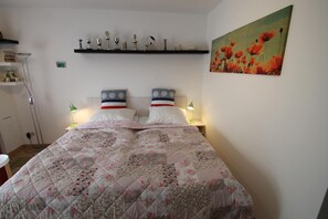 Una camera da letto con una coperta trapuntata a motivi floreali, due lampade ai comodini, uno scaffale con trofei e un quadro con papaveri appeso al muro.