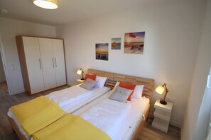 Un lit double avec deux tables de chevet, une armoire en bois et trois œuvres d’art murales.