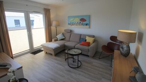 A modern living room with a sofa, a coffee table, and a lamp. There is a painting on the wall and a window with curtains.