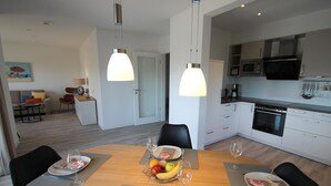 A modern kitchen with white cabinets, a microwave, and an oven. There is a dining area with a wooden table set for two, featuring plates, glasses, and a fruit bowl.