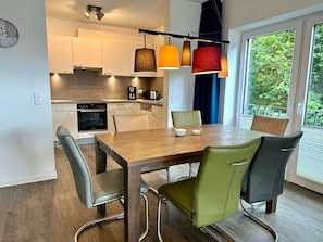 Una cocina moderna con armarios blancos, horno integrado y comedor con mesa y sillas de madera.