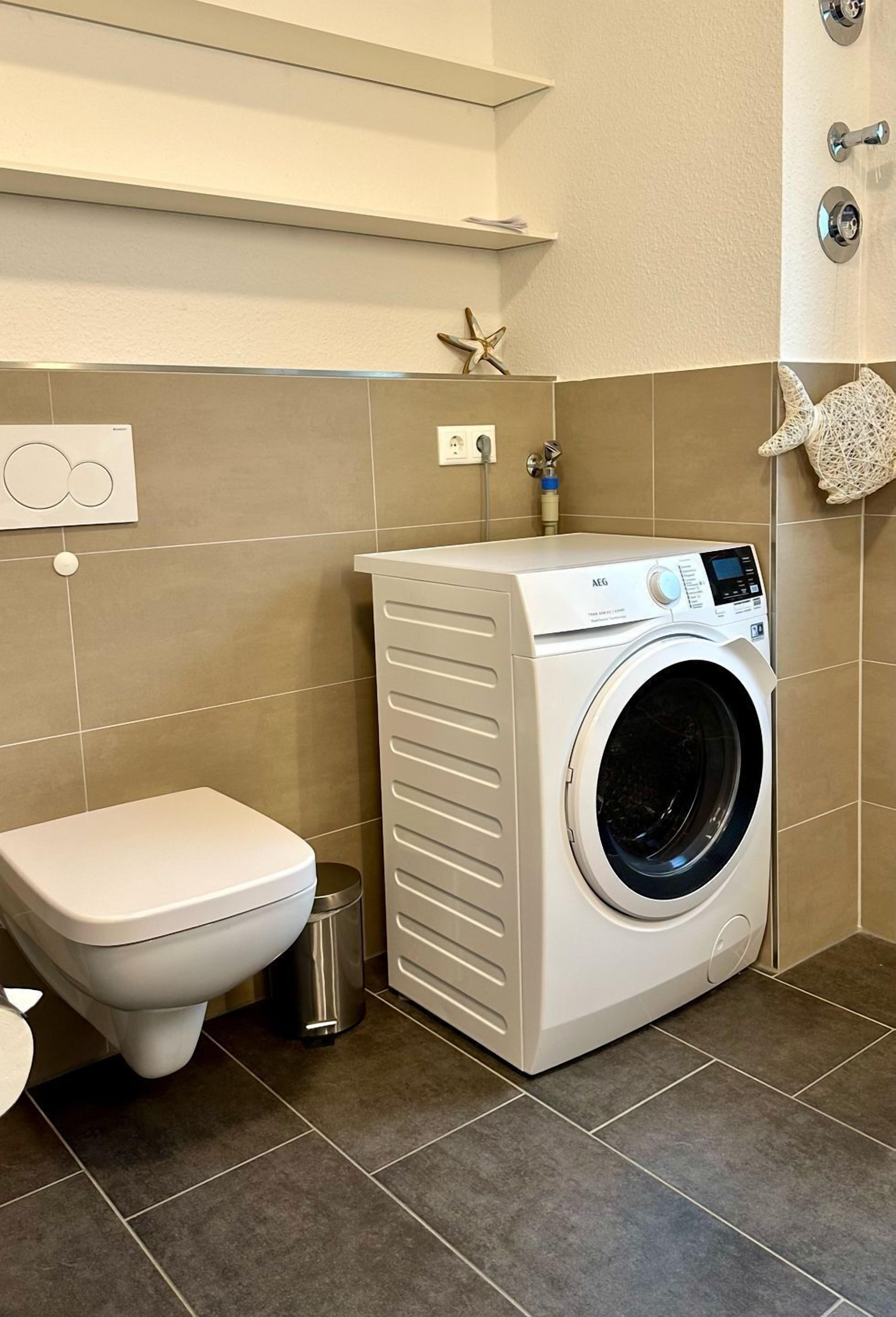 Een compacte badkamer met een wit toilet, een voorlader wasmachine en een kleine prullenbak.