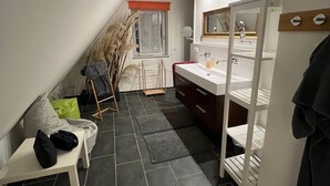 A compact, modern bathroom with a sloped ceiling, a white vanity with a mirror, and a shower area.