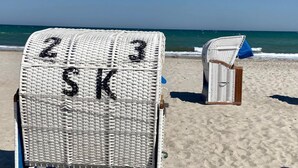 A beach chair with the letters "SK" on it, a second chair in the background, and the ocean in the distance.