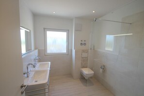 Ein modernes Badezimmer mit Doppelwaschbecken, Toilette und einer Duschkabine aus Glas.