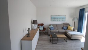 A modern living room with a sofa, armchair, coffee table, and a painting on the wall.
