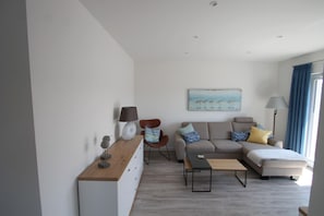 Un salon moderne avec un canapé, un fauteuil, une table basse et un tableau accroché au mur.