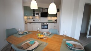 A modern kitchen with a dining table set for four, featuring a fruit bowl, wine glasses, and neatly arranged plates and cutlery.
