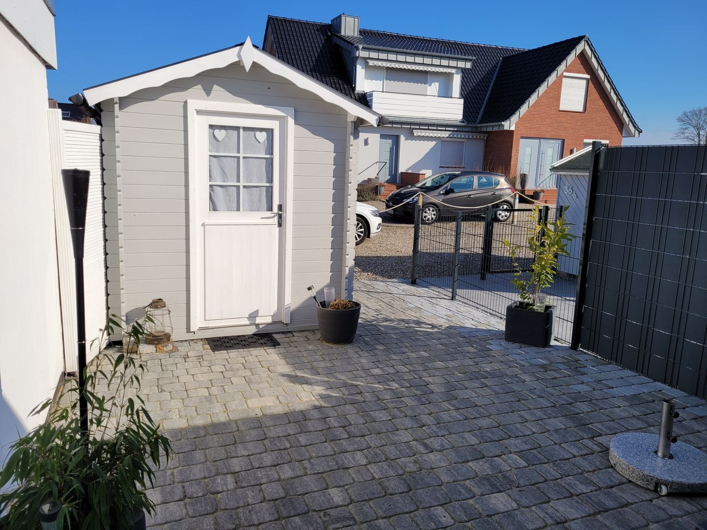 Un petit bâtiment blanc, de plain-pied, avec une porte et des fenêtres, une allée pavée et une voiture garée à l’arrière-plan.