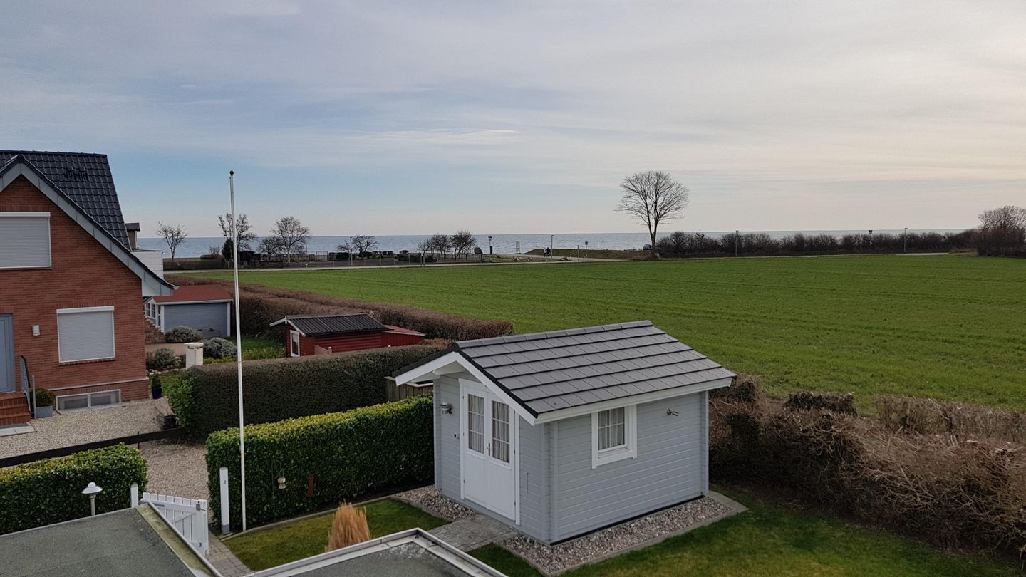 Een woonwijk met een kleine witte schuur, een bakstenen huis en een groot groen veld.