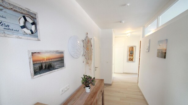 A hallway with a wooden bench, a wall-mounted life preserver, a framed picture of a sunset, and a door at the end. - 1805 - Ostseestern - 1805 - Ostseestern in Dahme (Dahme)