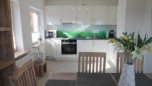 A modern kitchen with white cabinets, a microwave, and a sink. There is a wooden chair and a table with a vase of flowers. - 1805 - Ostseestern - 1805 - Ostseestern in Dahme (Dahme)