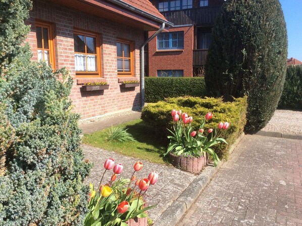 Casa de ladrillo con jardín que presenta tulipanes rojos y un seto bien cuidado.