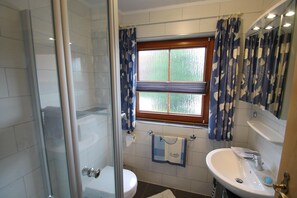 Un baño con cabina de ducha de vidrio, inodoro, lavamanos y ventana con cortinas.