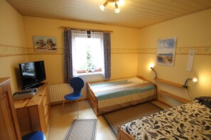 A small, cozy room with a bed, a desk with a TV, a chair, and a window with curtains.
