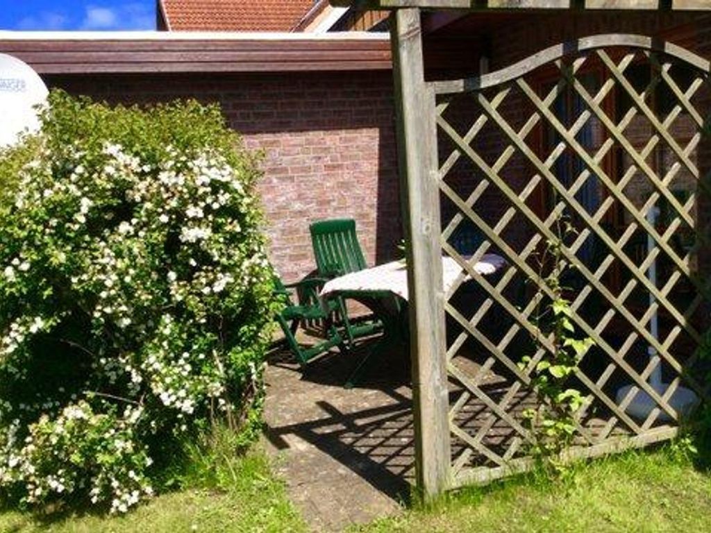 Un jardín con un portón de madera con celosía, una silla verde y un arbusto de flores blancas.