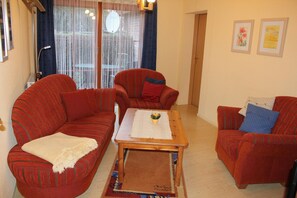 Una sala de estar con un sofá rojo, un sillón más pequeño y una mesa de centro de madera.