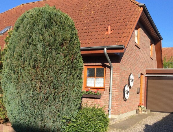 Una casa de ladrillo con techo de tejas, un gran árbol de hoja perenne al frente y una puerta de garaje.