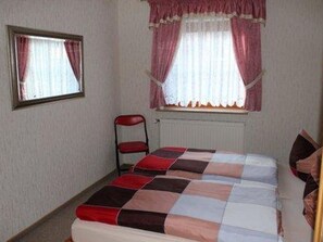 Un dormitorio con una cama, una silla y un ventanal con cortinas.