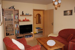 A cozy living room with a sofa, a television, a wooden coffee table, and a bookshelf filled with books and decorative items.
