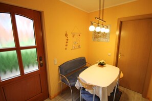 Un comedor con una mesa, sillas, un banco, una puerta con paneles de vidrio esmerilado y una lámpara fijada a la pared.