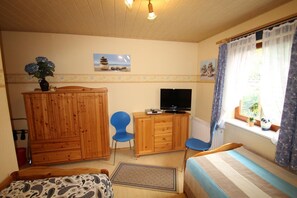 Una habitación acogedora con cama, escritorio con televisor, armario y ventana con cortinas.