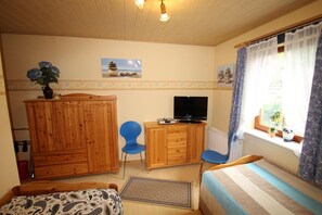 Una habitación acogedora con cama, escritorio con televisor, armario y ventana con cortinas.