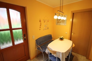Un comedor con una mesa, sillas, un banco, una puerta con paneles de vidrio esmerilado y una lámpara fijada a la pared.