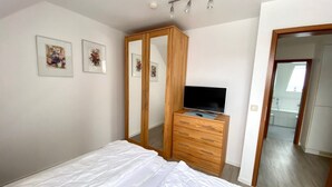 A bedroom with a bed, a wooden dresser, a TV on top, and a mirror cabinet. - 2050 - House Heisterbusch (Kellenhusen (Ostsee))
