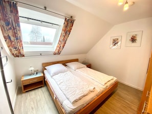 Une chambre avec un lit simple, une table de chevet, une fenêtre avec des rideaux et un luminaire au plafond.