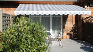 A patio with a metal chair and a table, a brick house with a tiled roof, and a metal gate. - 2050 - House Heisterbusch (Kellenhusen (Ostsee))