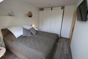 A bedroom with a bed, pillows, a nightstand, a lamp, a wardrobe, and a television.