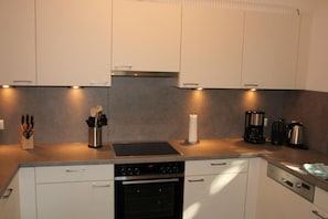 A modern kitchen with white cabinets, a stainless steel range hood, a built-in oven, a sink, and various appliances including a coffee maker and a kettle.