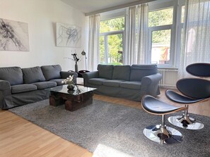 Ein modernes Wohnzimmer mit zwei grauen Sofas, einem Glastisch und einem einzigartigen Sessel mit Metallfuß.
