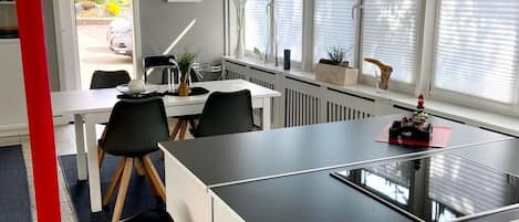 A modern kitchen with a central island, white cabinetry, and a dining area with chairs and a table.